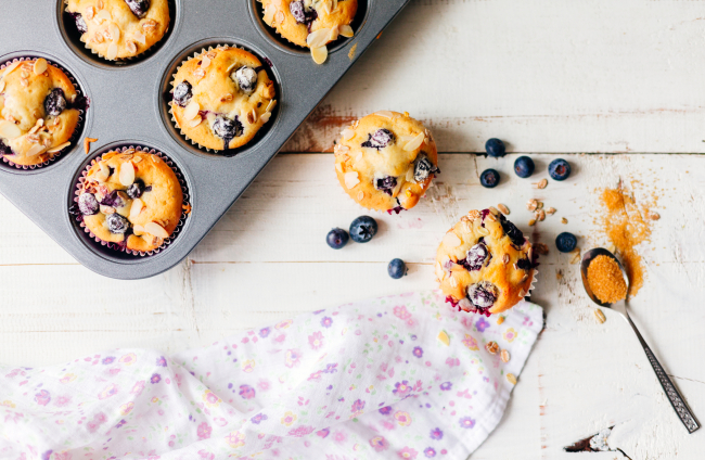 Freshly baked blueberry muffins with almond, oats and icing sugar topping on a rustic white wooden table  with berries, brown sugar. Top view
