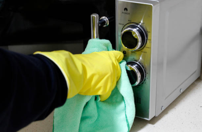 Close-up of hand with rubber glove cleaning microwave