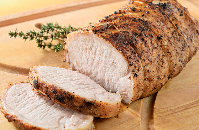 "Herb crusted pork tenderloin roast being sliced on a cutting board, warm from the oven.  Thyme garnish.  Very shallow DOF.