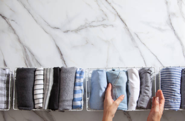 Neatly folded clothes and pyjamas in the metal mesh organizer basket on white marble table. modern style of garments declutter and sorting concept. Housewife using modern method of tidying up