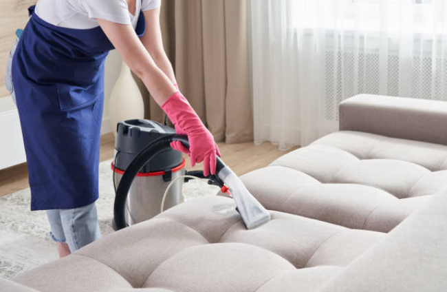 Woman Cleaning Sofa With Vacuum Cleaner At Hom