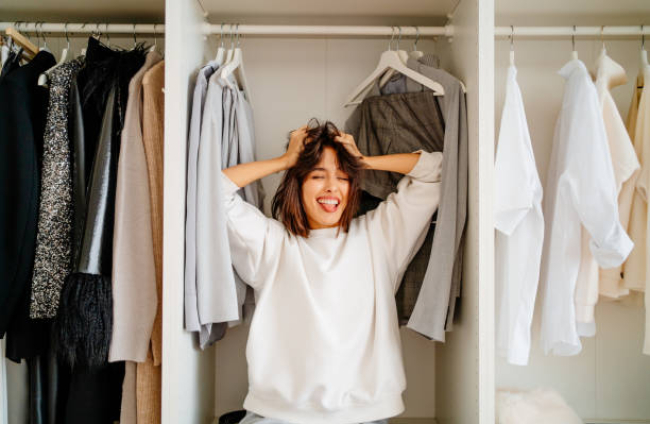Playful funny dark bobbed haired woman posing in the wardrobe among clothes racks. What to wear, help m