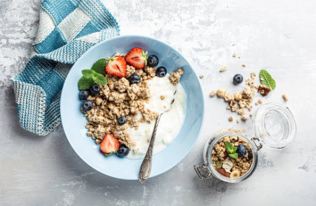 Overhead schoot of granola with nuts mix, yogurt, fresh berries and honey on blue plate voor healthy breakfast, top view, copy space