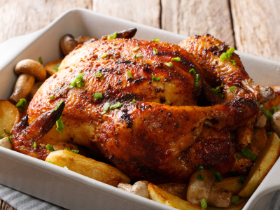 Whole grilled chicken with mushrooms and potatoes close-up in a baking dish. horizontal