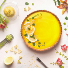 Yellow lemon tart topped with fresh lemon and lime slices on white table background with citrus ingredients and flowers, top view. Traditional french cuisin