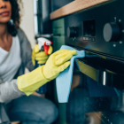 Shot of young woman cleaning the outside of an oven. Woman cleaning with spray disinfectant and gloves at home
