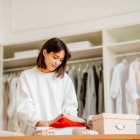 Brunette woman packing and stacking clothes items into the boxes in a big showroom or wardrobe room with a lot of clothing and shoes rack