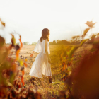 Portrait of young beautiful model in white dress resting in field at sunset