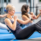 A middle aged caucasian woman shows a look of determination as she does an ab workout with a group of people in a gym