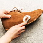 Hands cleaning men's camel suede desert shoe (boot) with a brush. Footwear maintenance captured from above (top view). Grey concrete background