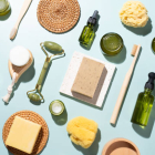 A Variety of Plastic Free and Zero Waste Toiletries and Beauty Products Made from Wood, Bamboo and Glass Materials, Which Include Essential Oil, Soap Bar, Natural Sponge, Jade Roller, Toothbrush, Hair Comb, Facial Cleanser and Moisturizer on Green Background High Angle View