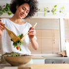 Happy young multiracial woman mixing a bowl of fresh salad.  Copy space.  Healthy lifestyle concept